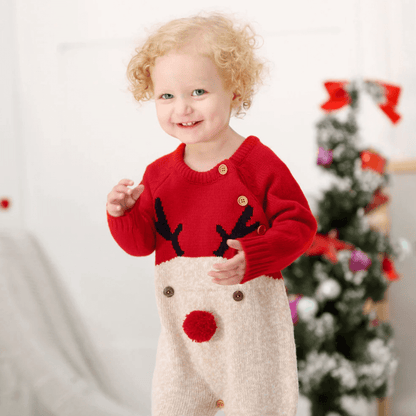 Bébé portant une combinaison de Noël rouge avec motif renne devant un sapin décoré.